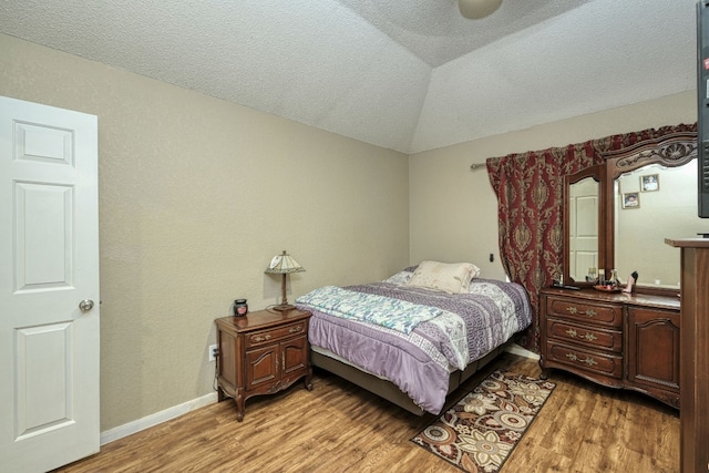 bedroom with vaulted ceiling, light hardwood / wood-style floors, and a textured ceiling