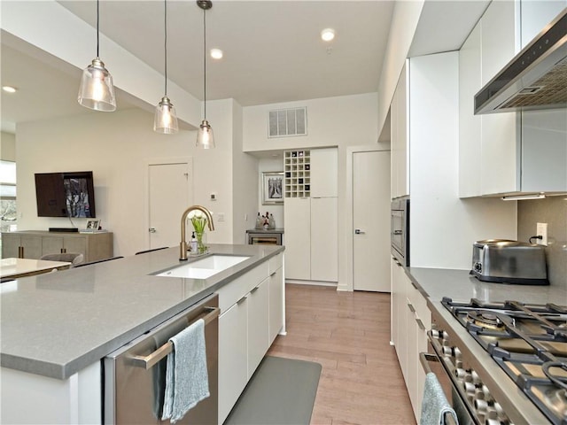 kitchen featuring stainless steel appliances, an island with sink, sink, white cabinetry, and range hood