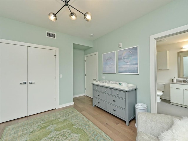 bedroom featuring light hardwood / wood-style flooring, a closet, connected bathroom, an inviting chandelier, and sink