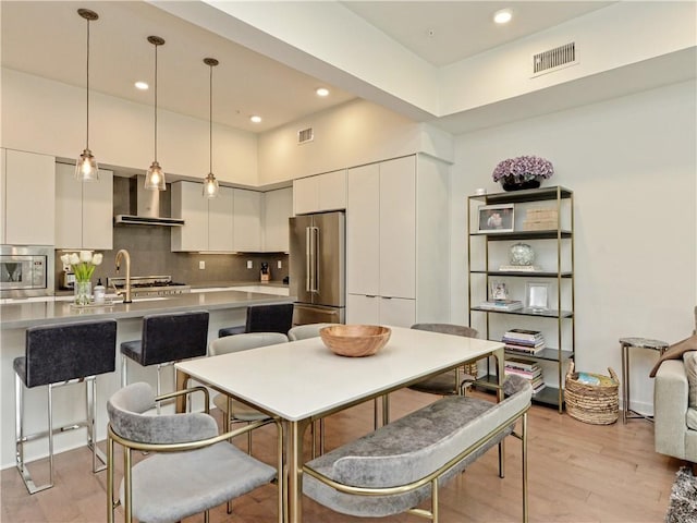 kitchen featuring white cabinets, wall chimney exhaust hood, a kitchen breakfast bar, hanging light fixtures, and appliances with stainless steel finishes