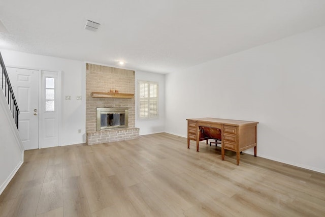 living room featuring brick wall, a brick fireplace, and light hardwood / wood-style flooring