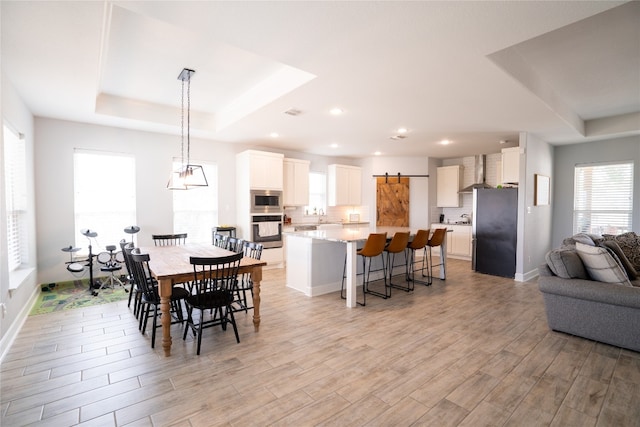 dining space featuring light hardwood / wood-style floors, sink, a chandelier, a tray ceiling, and a barn door