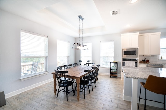 dining area with light hardwood / wood-style floors and a raised ceiling