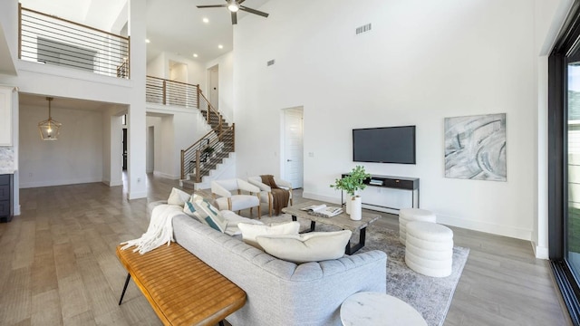 living room featuring hardwood / wood-style floors, ceiling fan with notable chandelier, and a high ceiling