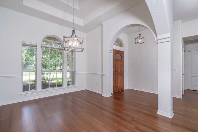 empty room with dark wood-type flooring, an inviting chandelier, and a raised ceiling