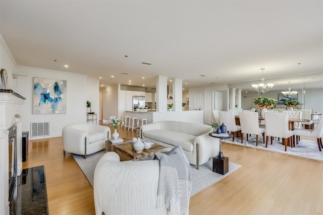 living area featuring a chandelier, visible vents, light wood-style floors, and a glass covered fireplace