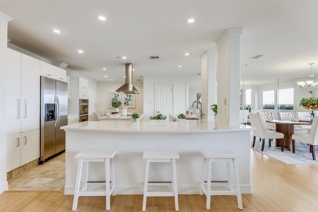 kitchen featuring visible vents, appliances with stainless steel finishes, island exhaust hood, a kitchen breakfast bar, and white cabinetry