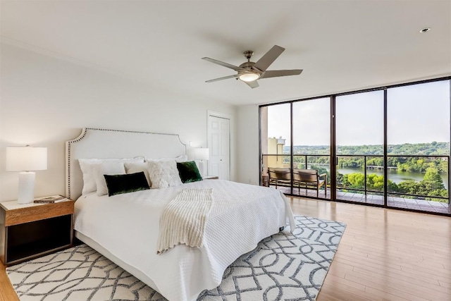 bedroom featuring a water view, a ceiling fan, floor to ceiling windows, light wood-style floors, and access to exterior