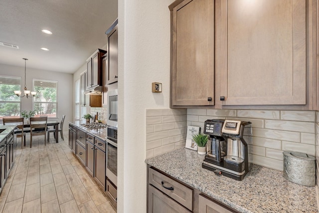 kitchen with appliances with stainless steel finishes, tasteful backsplash, light stone counters, and a notable chandelier