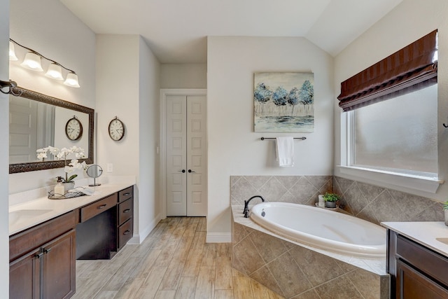 bathroom featuring hardwood / wood-style floors, vanity, lofted ceiling, and tiled tub