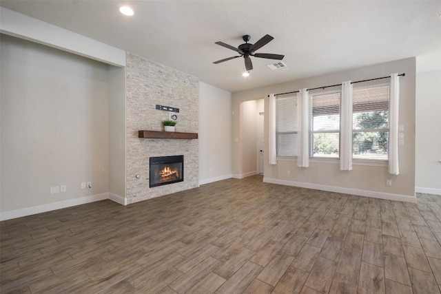 unfurnished living room featuring hardwood / wood-style flooring, ceiling fan, and a stone fireplace