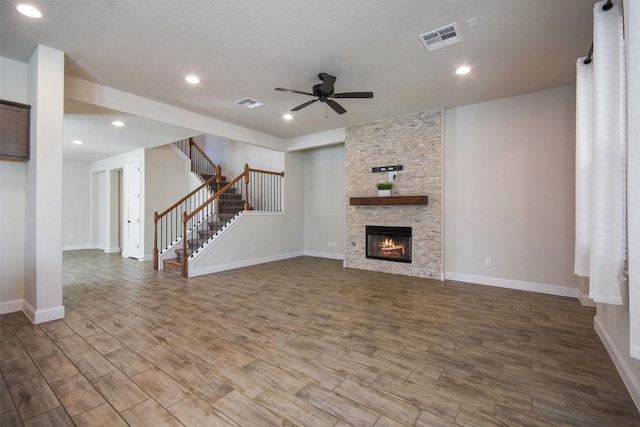 unfurnished living room with wood-type flooring, a stone fireplace, and ceiling fan