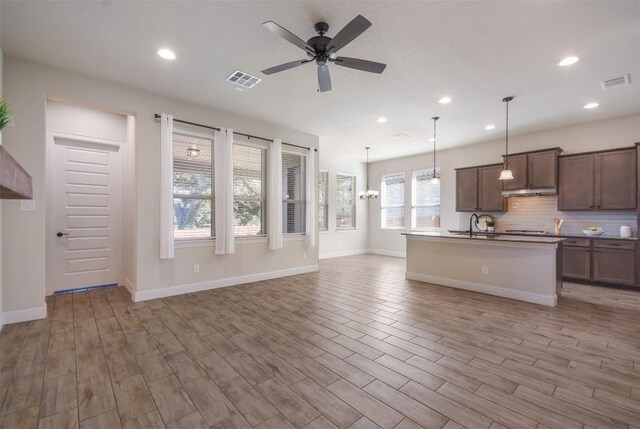 kitchen featuring ceiling fan, backsplash, an island with sink, decorative light fixtures, and light wood-type flooring