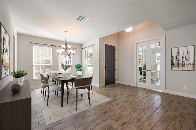 dining space with a textured ceiling, hardwood / wood-style floors, french doors, and a notable chandelier