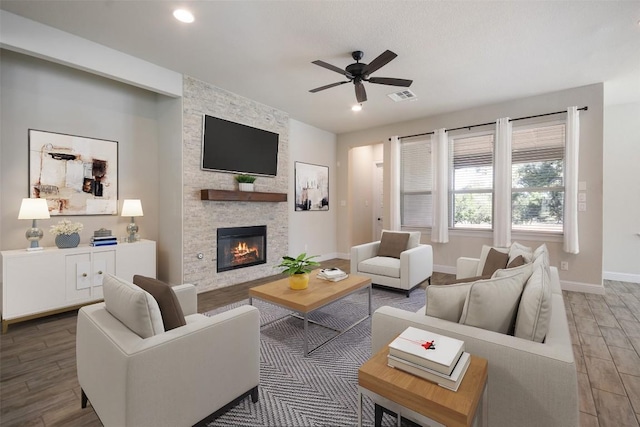 living room featuring ceiling fan, a stone fireplace, and wood-type flooring