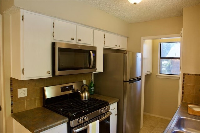 kitchen featuring stainless steel appliances, tasteful backsplash, tile floors, white cabinetry, and a textured ceiling