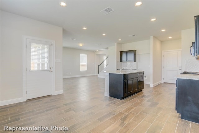 kitchen with backsplash, a kitchen island with sink, appliances with stainless steel finishes, and light hardwood / wood-style flooring