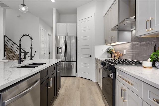 kitchen featuring sink, appliances with stainless steel finishes, hanging light fixtures, light stone countertops, and light wood-type flooring