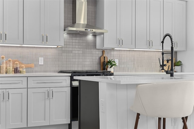 kitchen with wall chimney exhaust hood, a kitchen bar, decorative backsplash, and white cabinets