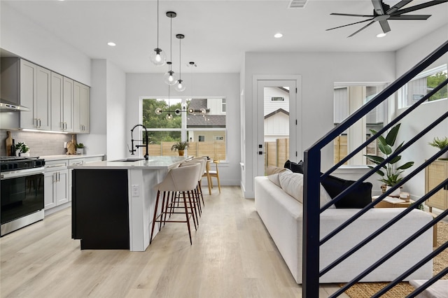 kitchen featuring sink, a kitchen breakfast bar, hanging light fixtures, a kitchen island with sink, and stainless steel gas range