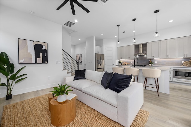 living room featuring ceiling fan, sink, and light wood-type flooring