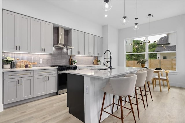 kitchen with sink, hanging light fixtures, a center island with sink, stainless steel range with gas stovetop, and wall chimney range hood