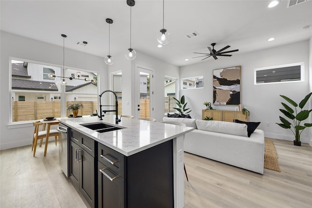 kitchen featuring sink, stainless steel dishwasher, pendant lighting, light stone countertops, and light hardwood / wood-style floors