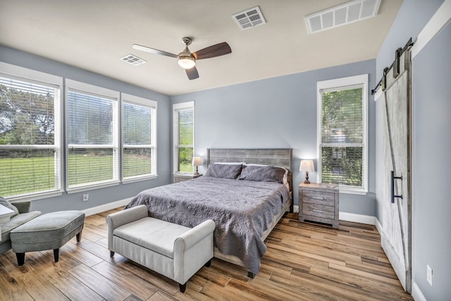 bedroom with ceiling fan, wood-type flooring, and a barn door