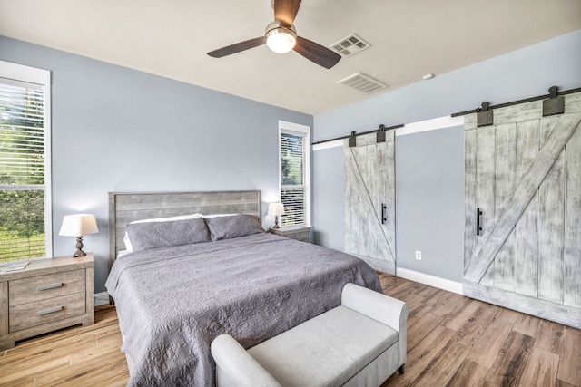 bedroom with a barn door, ceiling fan, and light wood-type flooring