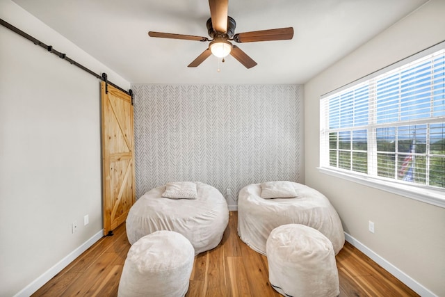 bedroom with a barn door, hardwood / wood-style flooring, and ceiling fan