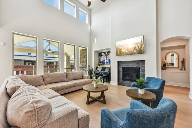 living room featuring a towering ceiling, light hardwood / wood-style floors, a fireplace, and ceiling fan