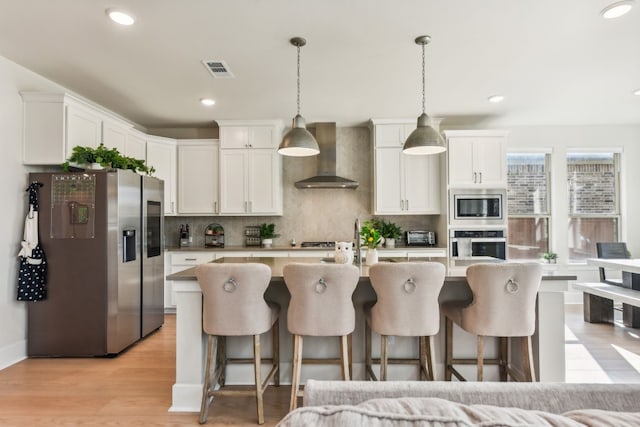 kitchen featuring light wood-type flooring, wall chimney exhaust hood, stainless steel appliances, and white cabinets