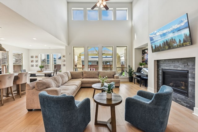 living room featuring a fireplace, a high ceiling, light hardwood / wood-style flooring, and a healthy amount of sunlight