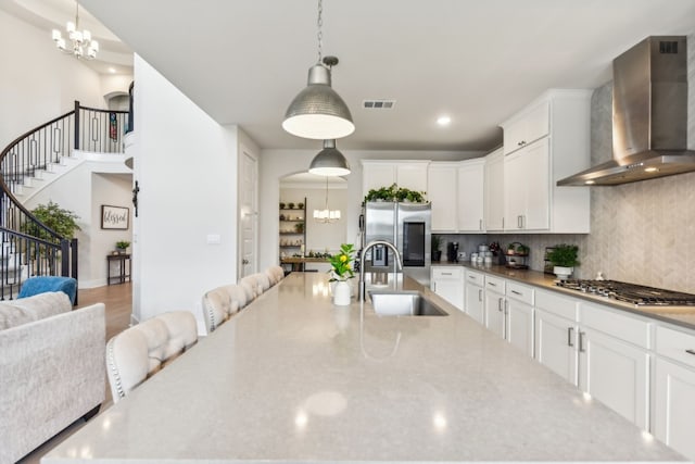 kitchen featuring wall chimney exhaust hood, sink, hanging light fixtures, appliances with stainless steel finishes, and white cabinetry