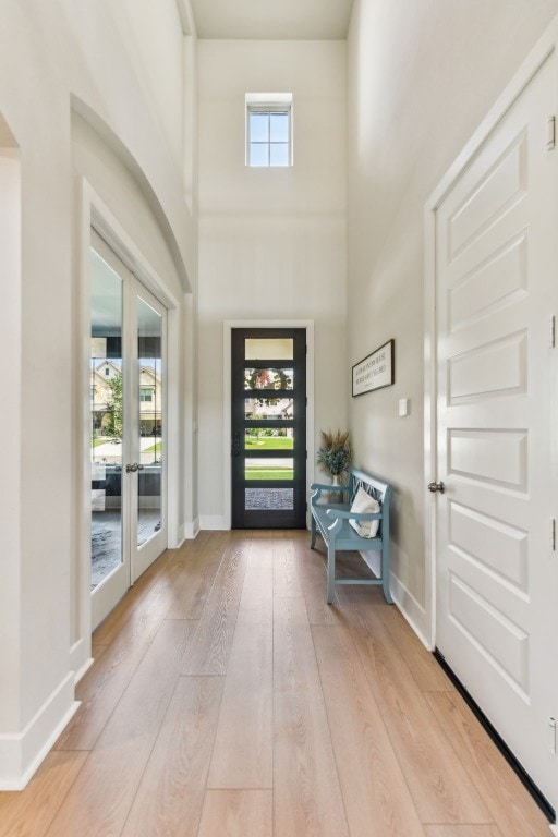 foyer with a towering ceiling, light wood-type flooring, plenty of natural light, and french doors