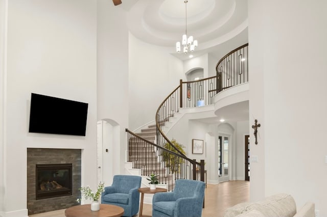 living room with a high ceiling, an inviting chandelier, a tiled fireplace, a raised ceiling, and hardwood / wood-style flooring