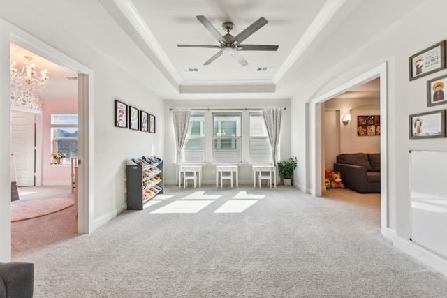 living area featuring ceiling fan with notable chandelier, plenty of natural light, a tray ceiling, and light colored carpet