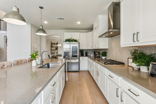 kitchen with white cabinets, pendant lighting, wall chimney exhaust hood, light hardwood / wood-style flooring, and appliances with stainless steel finishes