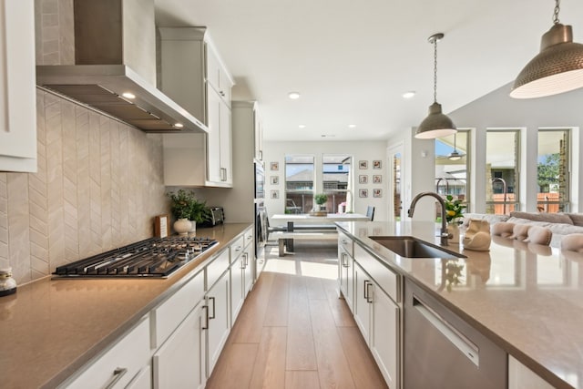 kitchen with wall chimney exhaust hood, light hardwood / wood-style floors, sink, stainless steel appliances, and hanging light fixtures