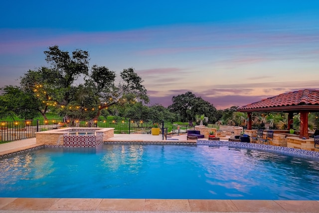 pool at dusk with a gazebo, an in ground hot tub, and a patio area