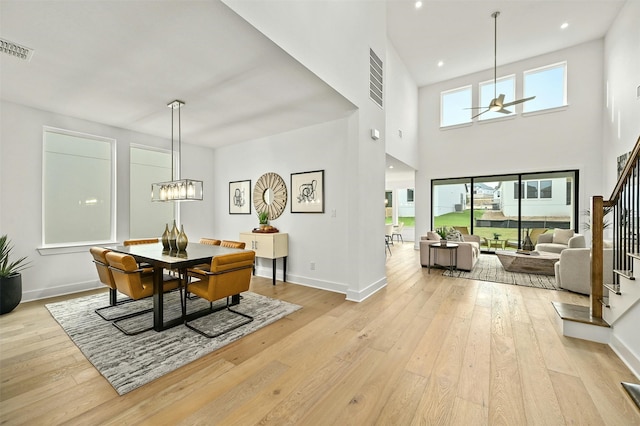 dining space featuring light wood-type flooring, ceiling fan with notable chandelier, and a high ceiling