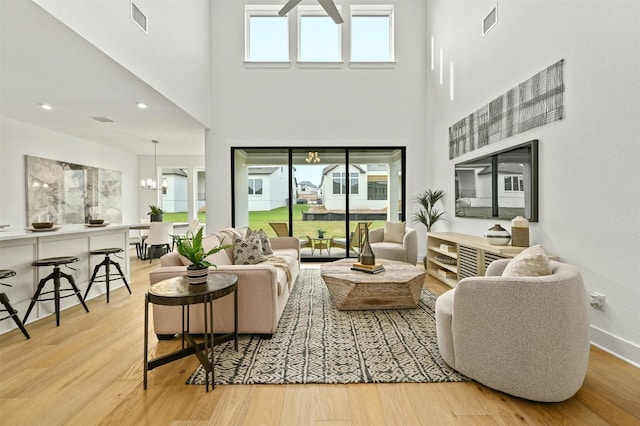 living room featuring light hardwood / wood-style floors, an inviting chandelier, and a high ceiling