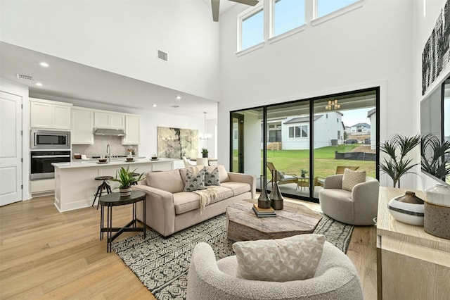 living room with a high ceiling, light wood-type flooring, sink, and a healthy amount of sunlight