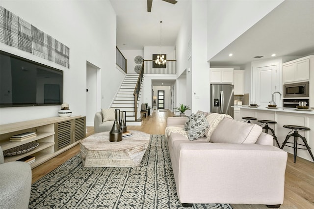 living room featuring light wood-type flooring, a towering ceiling, and ceiling fan