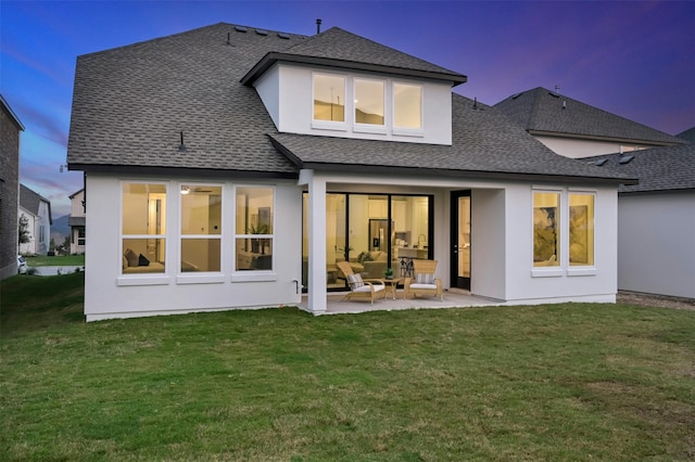 back house at dusk featuring a lawn and a patio