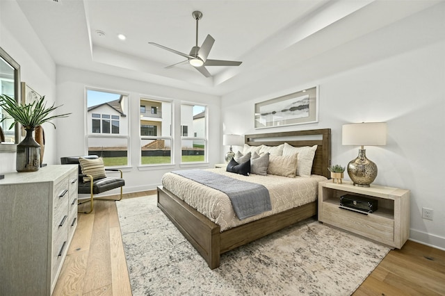 bedroom featuring light wood-type flooring, ceiling fan, and a tray ceiling