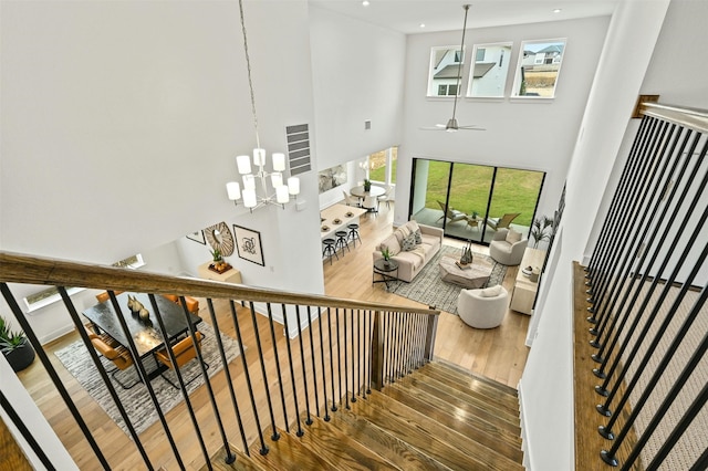 stairway featuring hardwood / wood-style flooring, a towering ceiling, and ceiling fan with notable chandelier