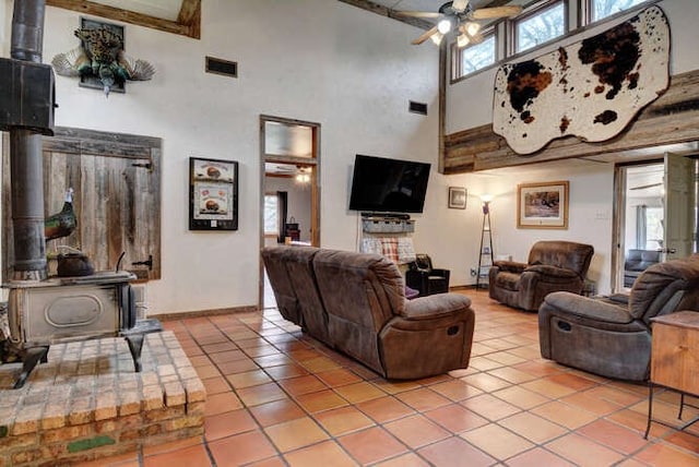 tiled living room featuring a towering ceiling, ceiling fan, and a wood stove