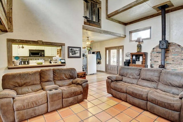 tiled living room featuring beam ceiling, a high ceiling, a wood stove, and french doors