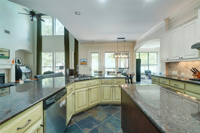 kitchen with stainless steel dishwasher, ceiling fan with notable chandelier, sink, dark stone countertops, and hanging light fixtures